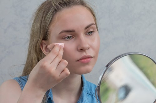 Caucasian girl applies alcohol on face 