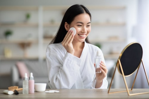 Cheerful asian woman cleaning her face with cleanser