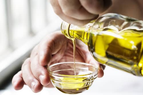 Bottle of olive oil being poured on small bowl