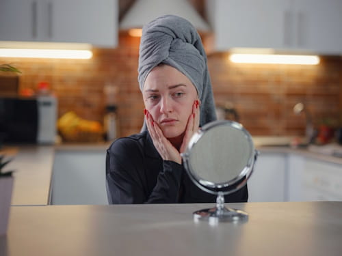 Woman worriedly looking at her skin with table mirror