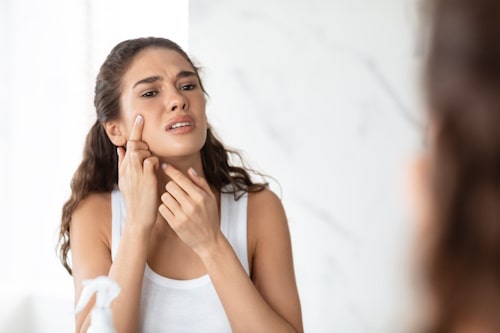 Desperate lady squeezing pimple on face near mirror