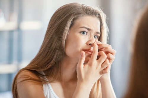 Woman picking pimple on nose with mirror