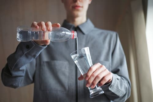 Young man pouring clean water to glass from bottle