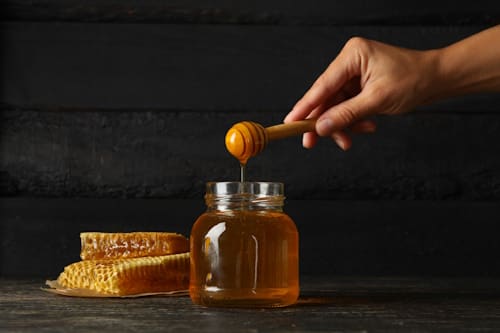 Person getting honey from jar of honey