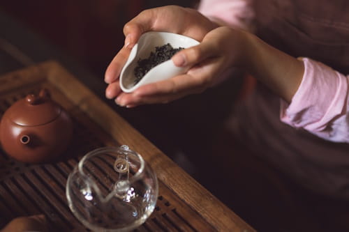 Person preparing green tea with tea pot and leaves