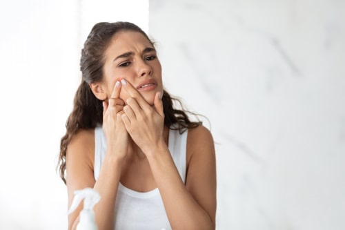 Frustrated lady with acne problem squeezing pimple 