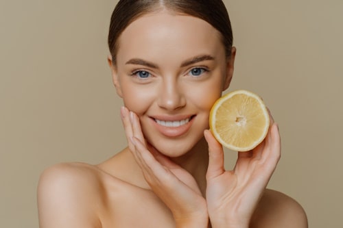 Woman holding cut lemon near her face