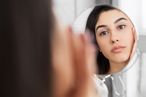 Woman looking at face with small table mirror
