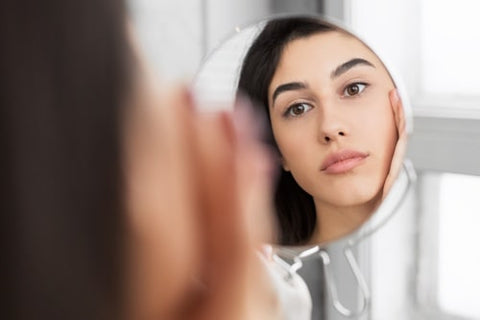 Woman looking at her face skin with mirror