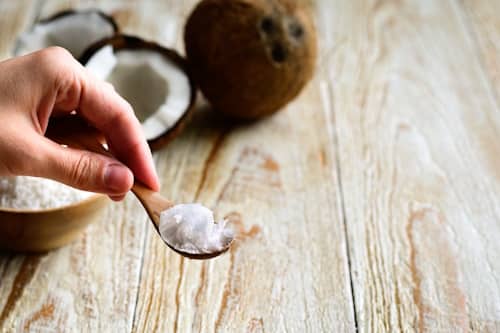 Spoon of coconut oil on spoon infront of coconut husks