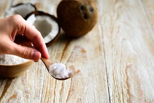 Coconut oil on spoon with coconuts in background