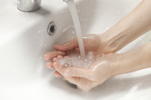 Hands cupping running water under bathroom sink