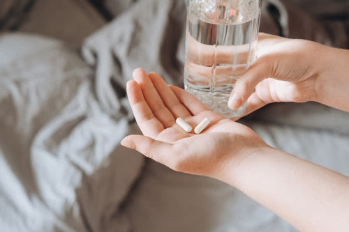 Hands of young woman holding Pantothenic acid and glass of water