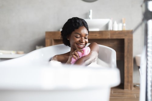 Happy young black lady taking foamy bath exfoliation