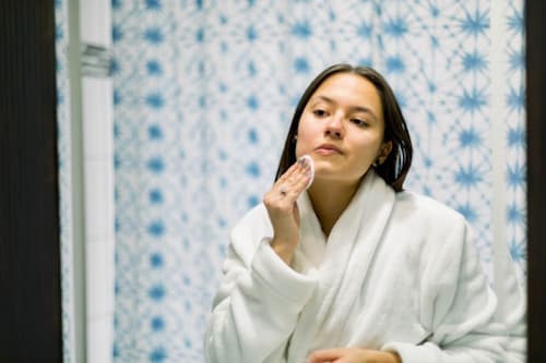 Using cotton pad to apply exfoliating serum on face