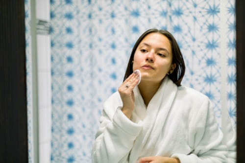 Hispanic woman in front of a mirror cleaning her face