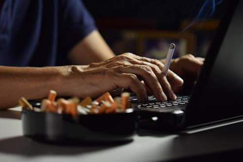 Man smoking cigarette by computer