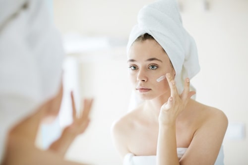 Woman with towel on head applying skin care product