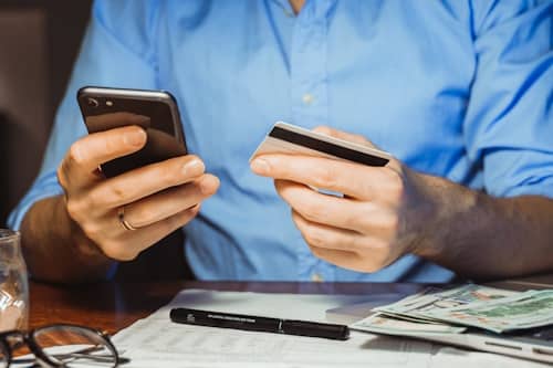 Man holding a credit card and cellphone worried about money