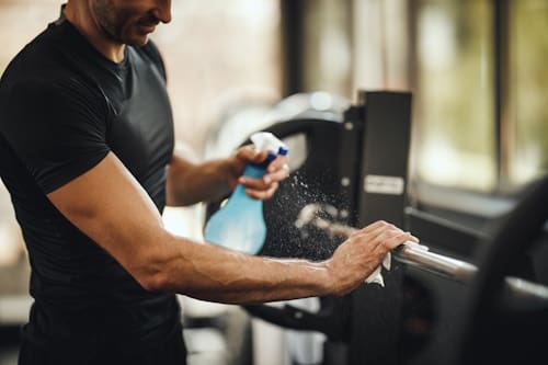 Man cleaning barbells using alcohol and towel