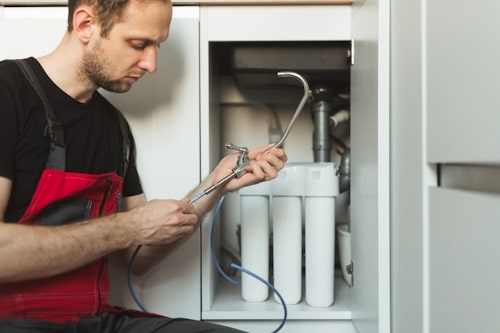 Plumber in the kitchen installs tap for household 