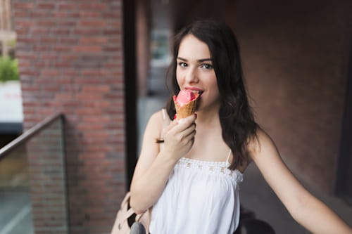 Young woman eating pink ice cream in cone