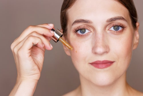 Portrait of young woman holding dropper with serum 