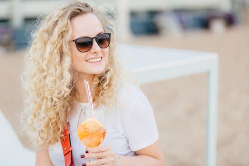 Woman with long hair wearing sun glasses drinking from a glass