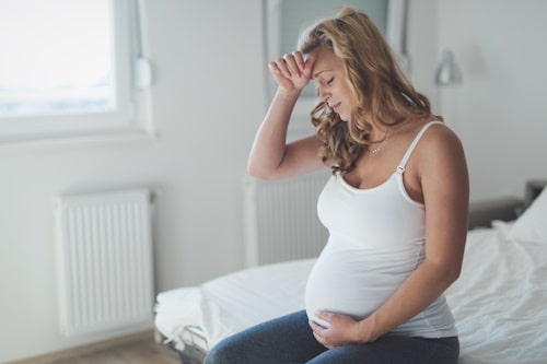 Stressed pregnant woman sitting on bed