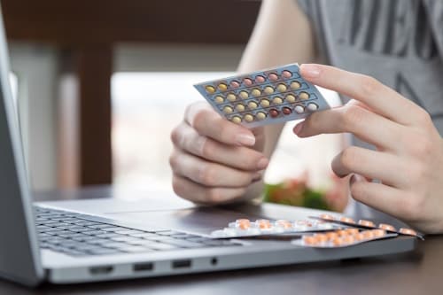 Woman holding Sprintec pill in front of laptop