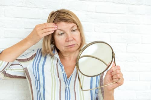 Senior woman checking her skin with hand mirror