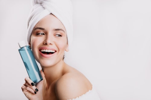 Woman happily places bottle fo micellar water on face