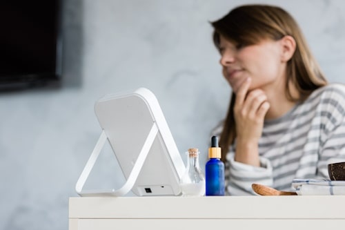 Woman looking at her face with table mirror not using skin care products