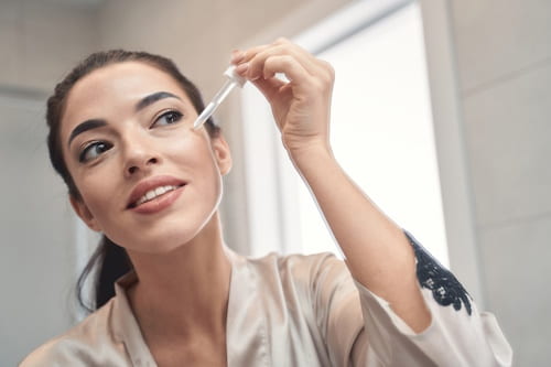 Woman happily adding serum to her face skin