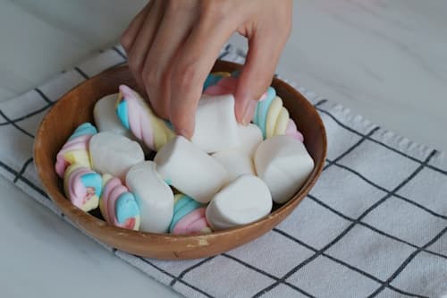 Hands of person getting marshmallows from bowl