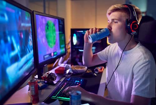 Young male teen drinking energy drink playing computer