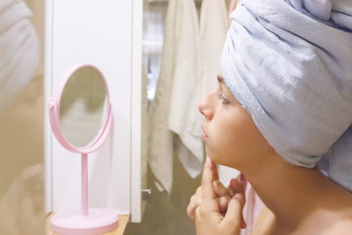 Girl checking her skin for pimples using table mirror