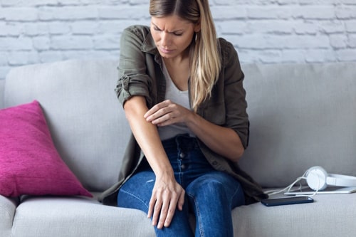 Uncomfortable young woman scratching her arm with acne