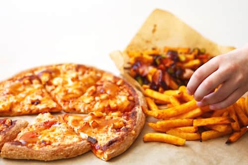 Hand grabbing fries with pizza and meat