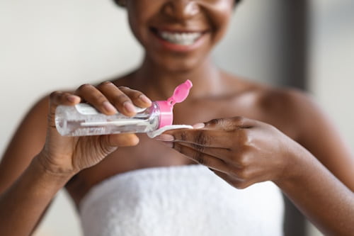 Torso level image of woman pouring micellar water onto cotton pad