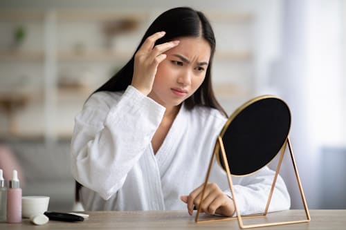 Woman looking at small mirror not happy with effects of mandelic acid