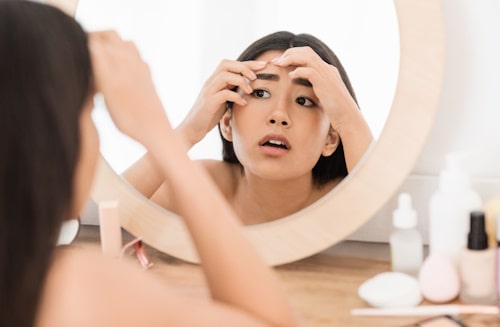 Asian woman looking at mirror with pimple