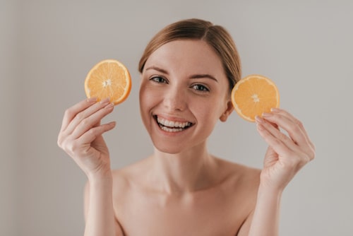 Woman holding two slices of orange happily