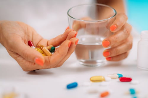 Different vitamin supplements spread out on a table with hand holding glass of water
