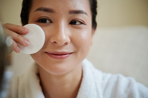 Image of woman applying micellar water on face while smiling
