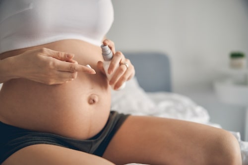 Pregnant woman applying moisturizer on tummy