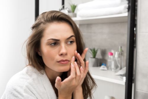 Woman looking at her dry skin with a mirror