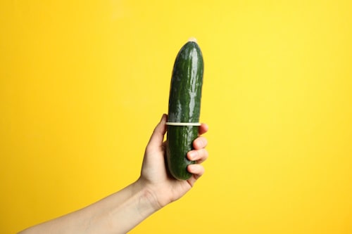 Hand holidng a cucumber with condom