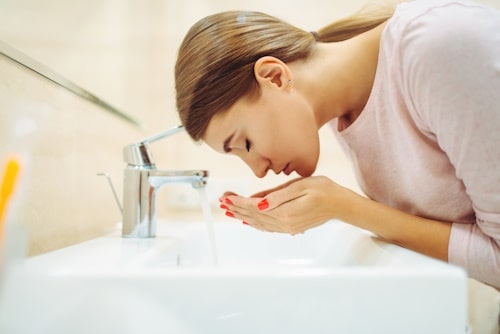 Woman washing her face after oil cleanse