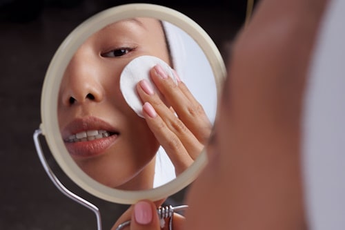 Asian woman putting makeup remover on face with mirror